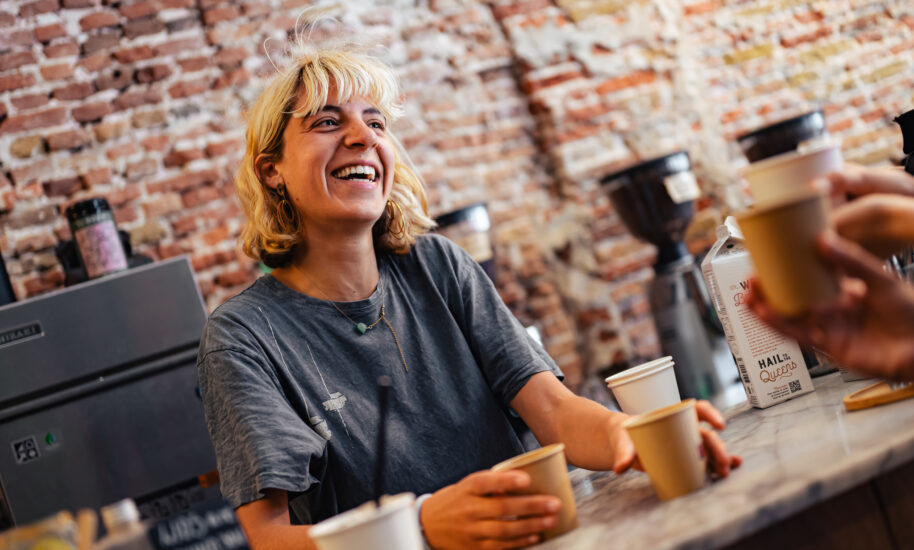 A smiling woman handing over a coffee cup. Barista serving coffee.
