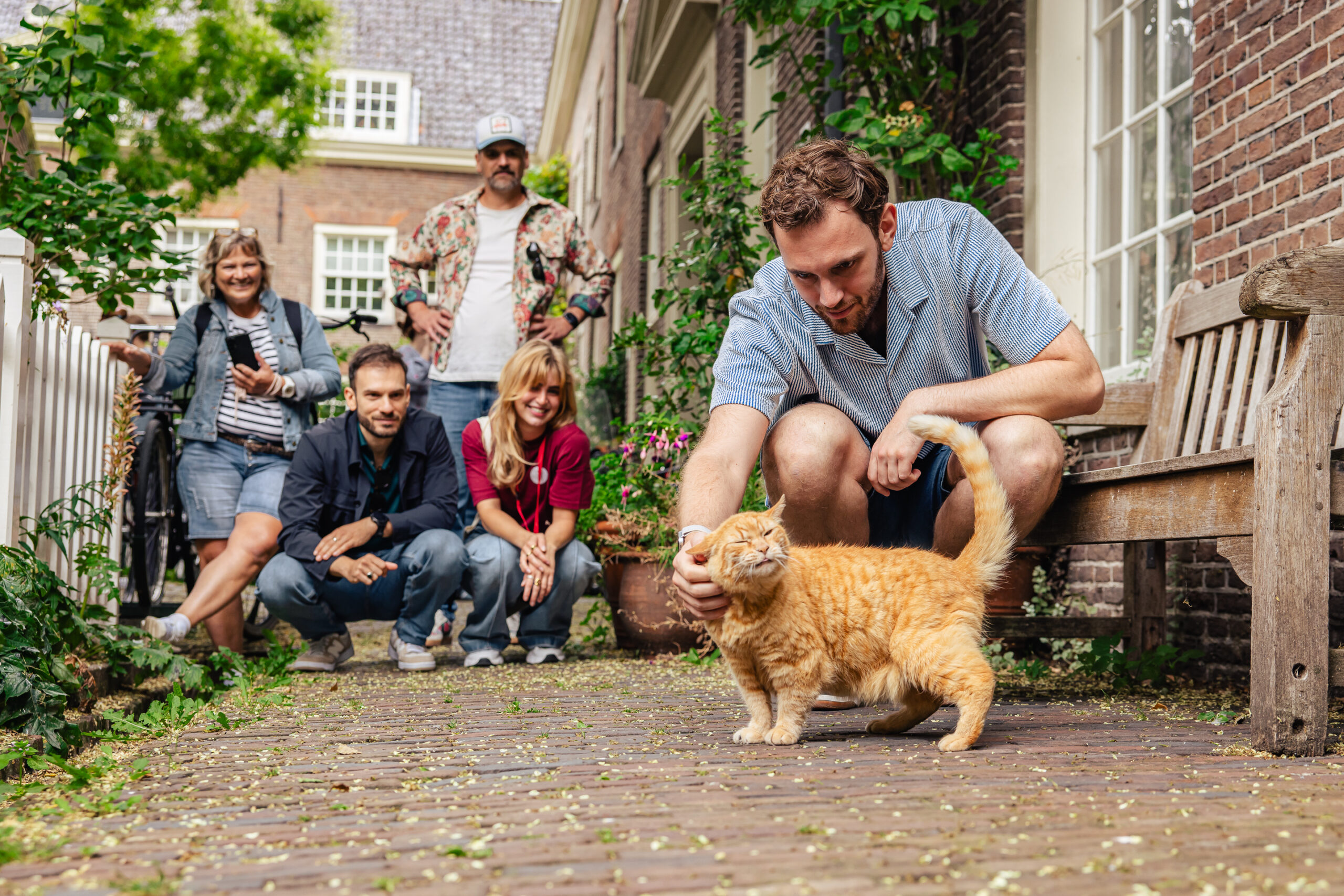 Tourist petting a cat while on a Jordaan Tour in Amsterdam. The tour group is in the Sint Andries Courtyard in Amsterdam.