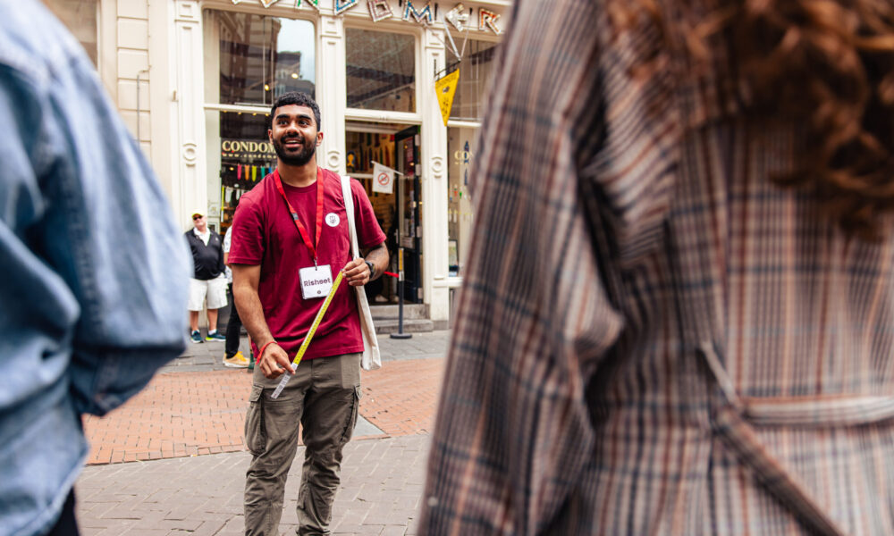 Tour guide in a red shirt and a name tag with the name Risheet on it guides a tour through the Red Light district.