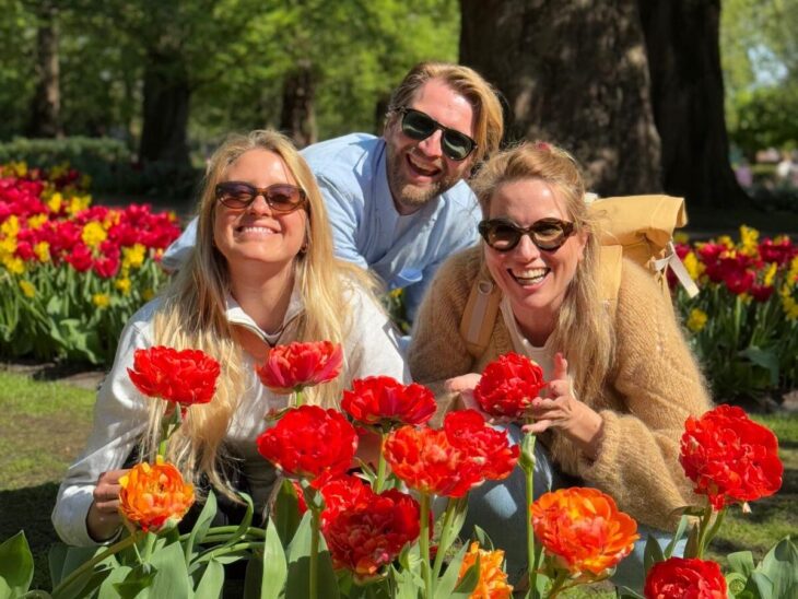 Three smiling tourists crouched among beautiful tulips. A perfect day out in Amsterdam.