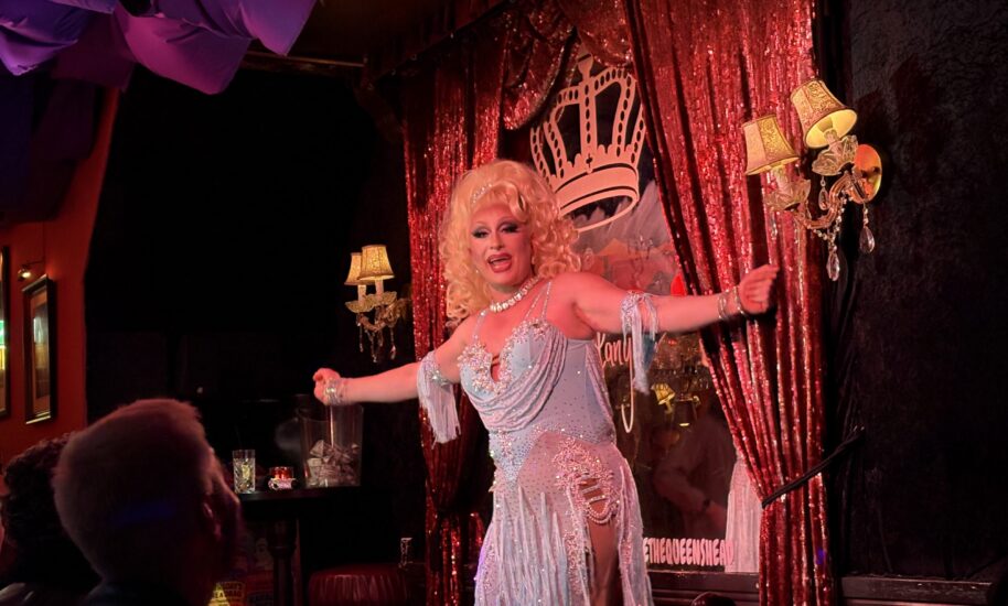 Drag Queen show café the queens head. Blonde performer in a white dress on stage. The performer appears to be in a theatrical setting.