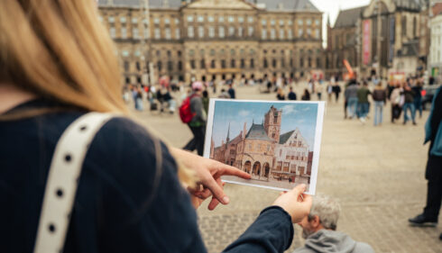 A tourist comparing a photo with a real building. Amsterdam city trip.