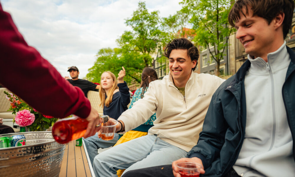 Friends on a boat in Amsterdam enjoying drinks. Group of young people smiling and having fun.